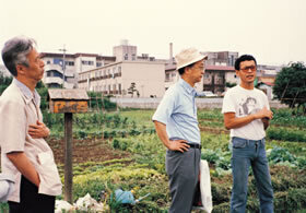 第3回研究コンクールの現地インタビューにて、やぼ耕作団（東京）《東京都下、国立市及び日野市内を主とする市街地周辺農地を利用した都市住民による自給農場運営の可能性に関する調査・研究》［83-3C-013］。左から小原秀雄選考委員、木原啓吉選考委員、やぼ耕作団代表の明峯哲夫氏、1985年6月